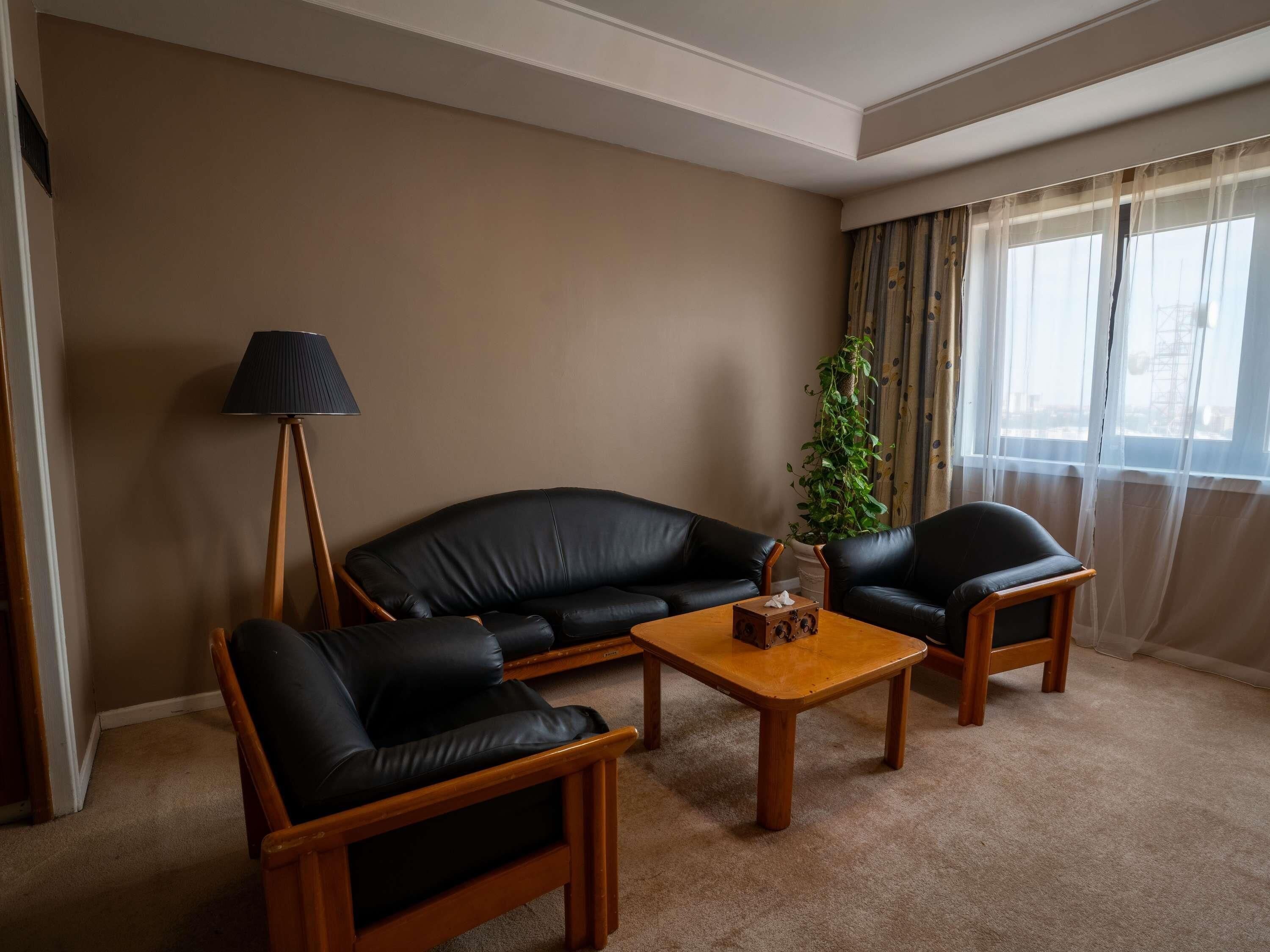 A living room with a sofa, two armchairs, a coffee table, a lamp, and a plant.