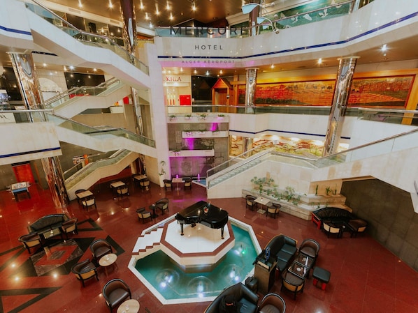 Un hall d’hôtel doté d’une piscine centrale, de plusieurs étages et offrant une vue sur l’aéroport d’Alger.