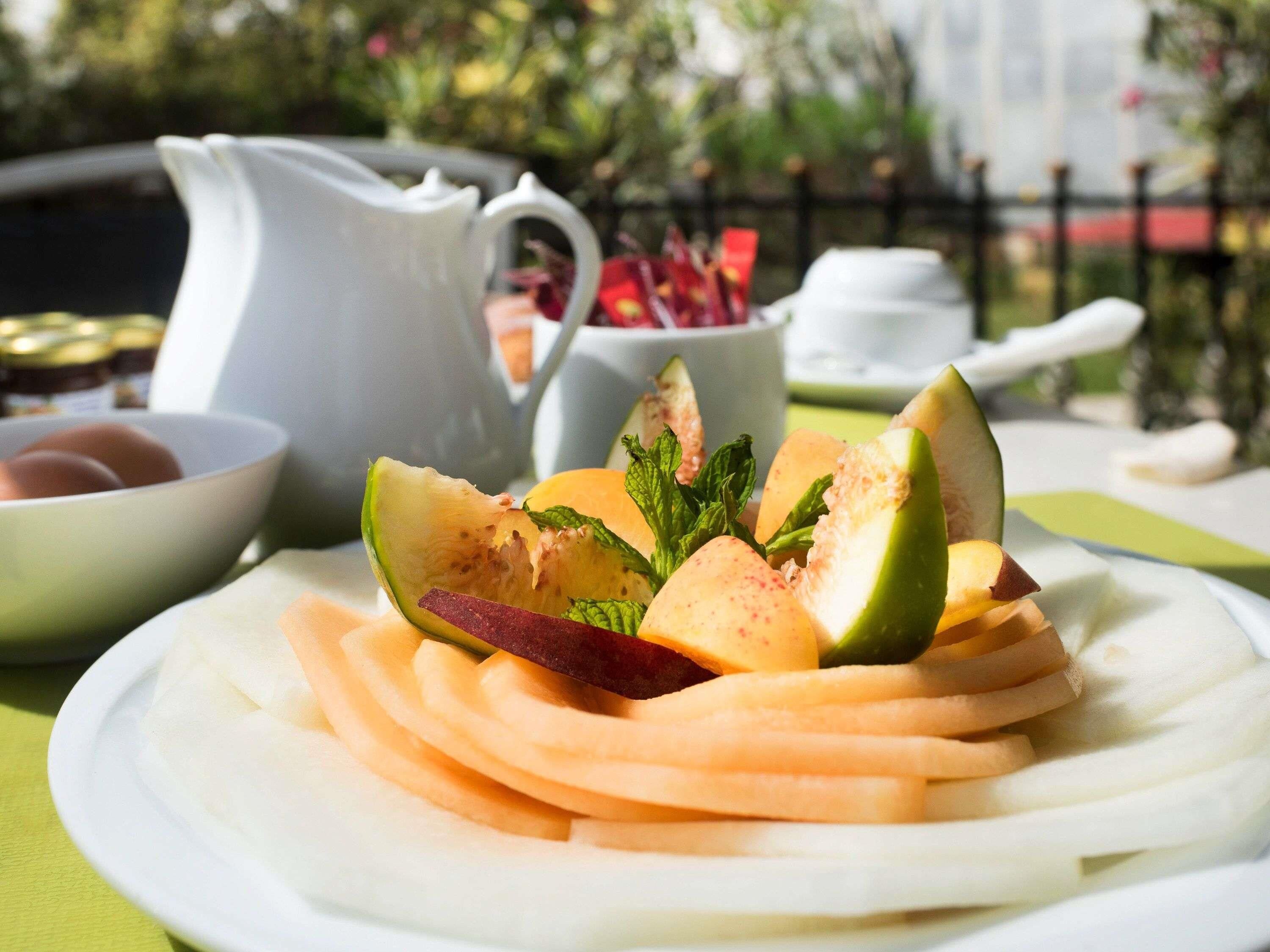 Un plato de frutas cortadas y una jarra blanca sobre una mesa con mantel verde.