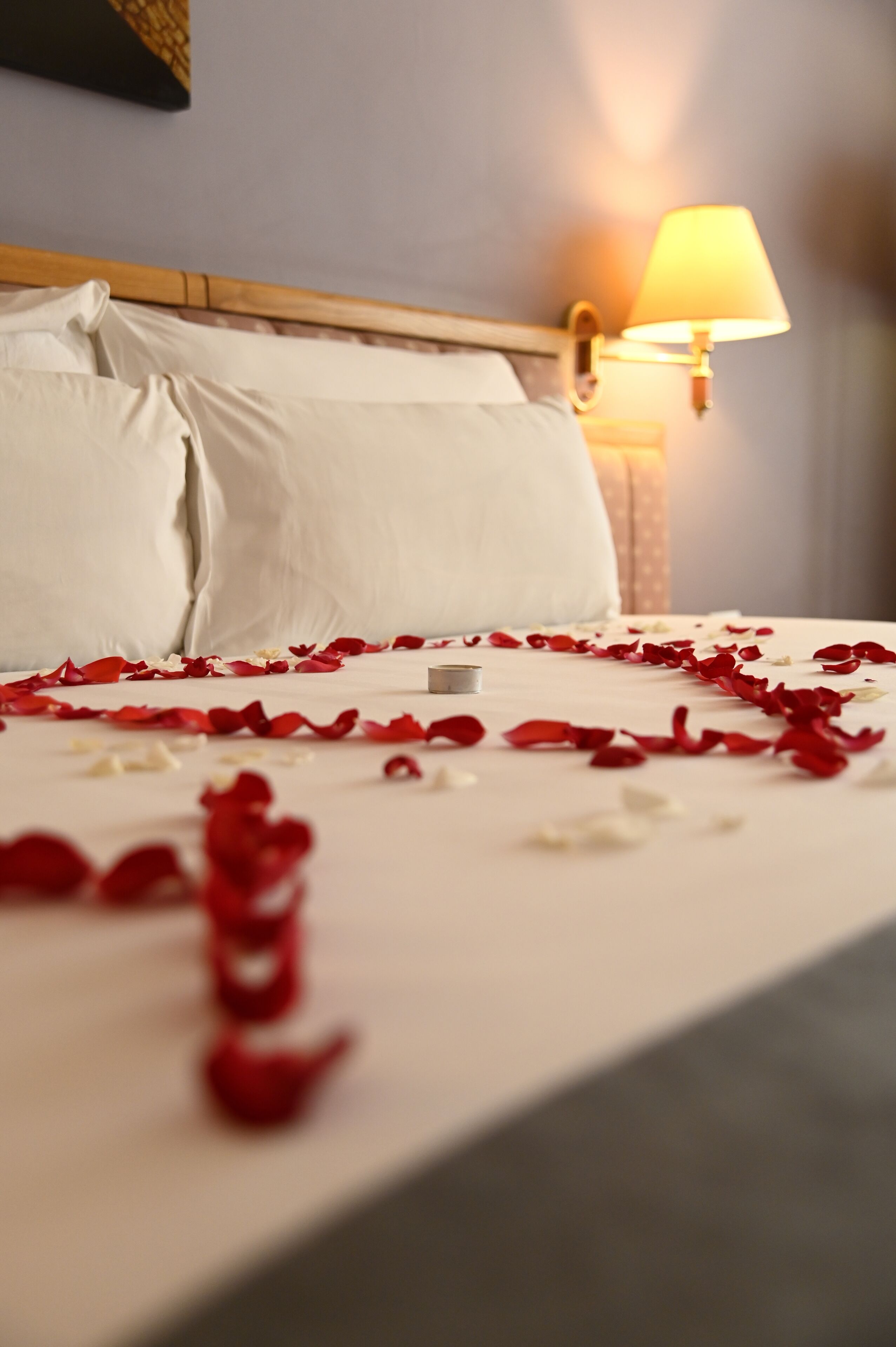 Un letto rifatto con cura, con lenzuola bianche e petali di rose rosse e bianche sparsi sopra.