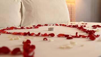 A neatly made bed with white linens and red and white rose petals scattered across it.