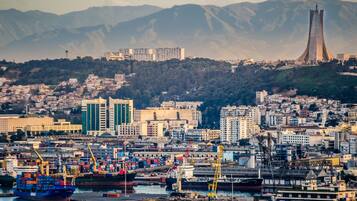 A coastal cityscape with a prominent tower, a busy port with cargo ships, and residential buildings.