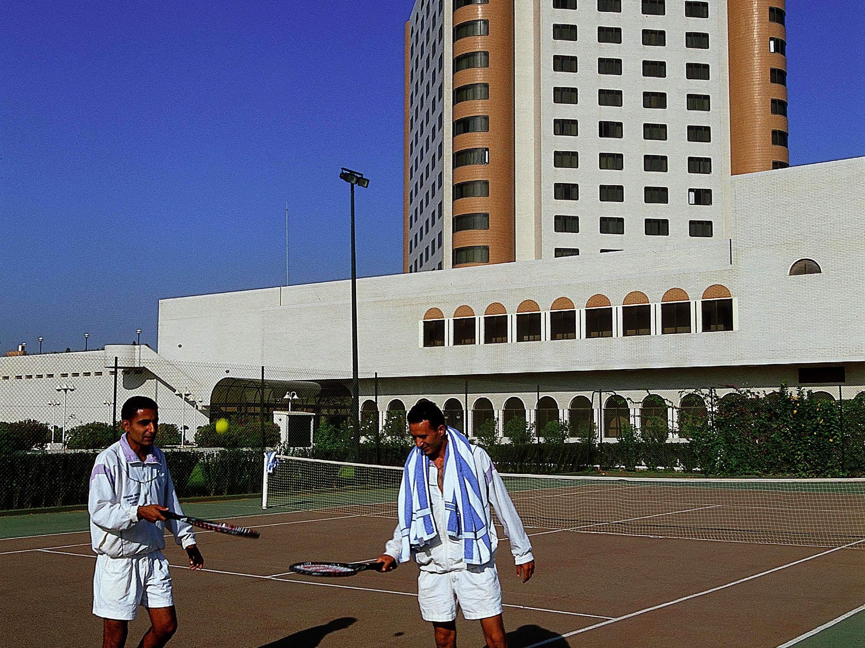 Una cancha de tenis con dos jugadores, una red y un edificio al fondo.