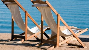 Two wooden beach chairs with canvas seats and backs, positioned on a sandy beach with a calm sea in the background. - Two Brothers Noordwijk Beach (Noordwijk)