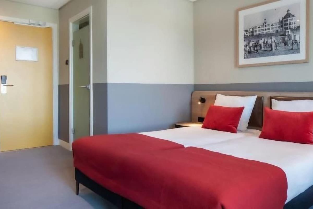 A hotel room with a large bed, two bedside tables, a door, and a framed picture on the wall.