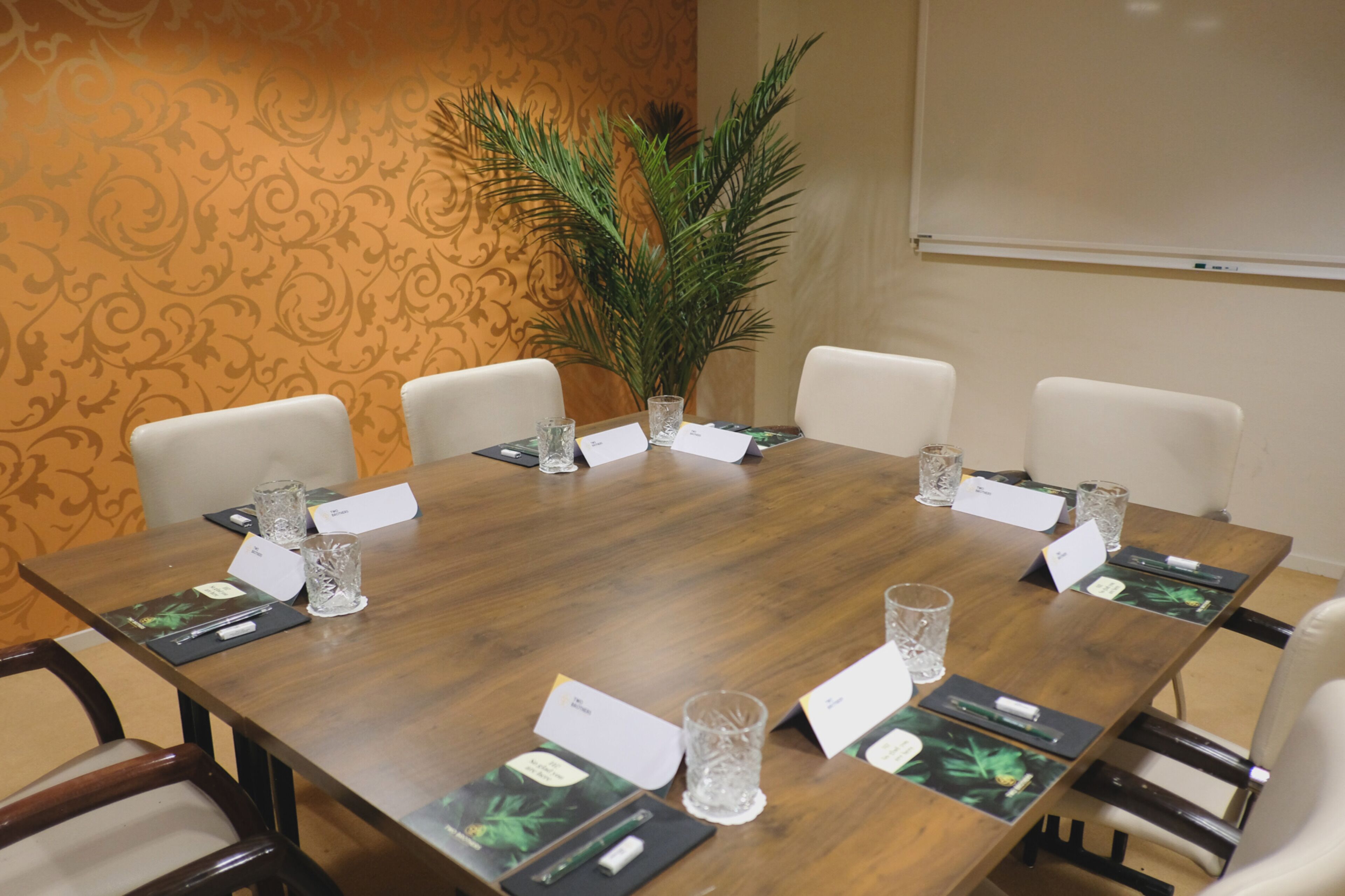 Een vergaderzaal met een houten tafel, witte stoelen, plaatskaarten en een potplant.
