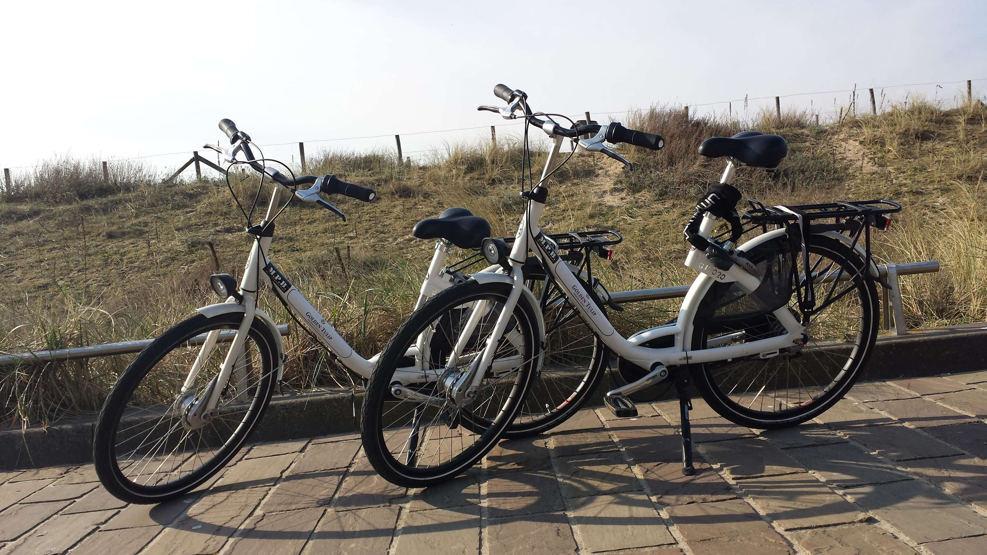 Three bicycles parked on a paved area with a grassy hill in the background.