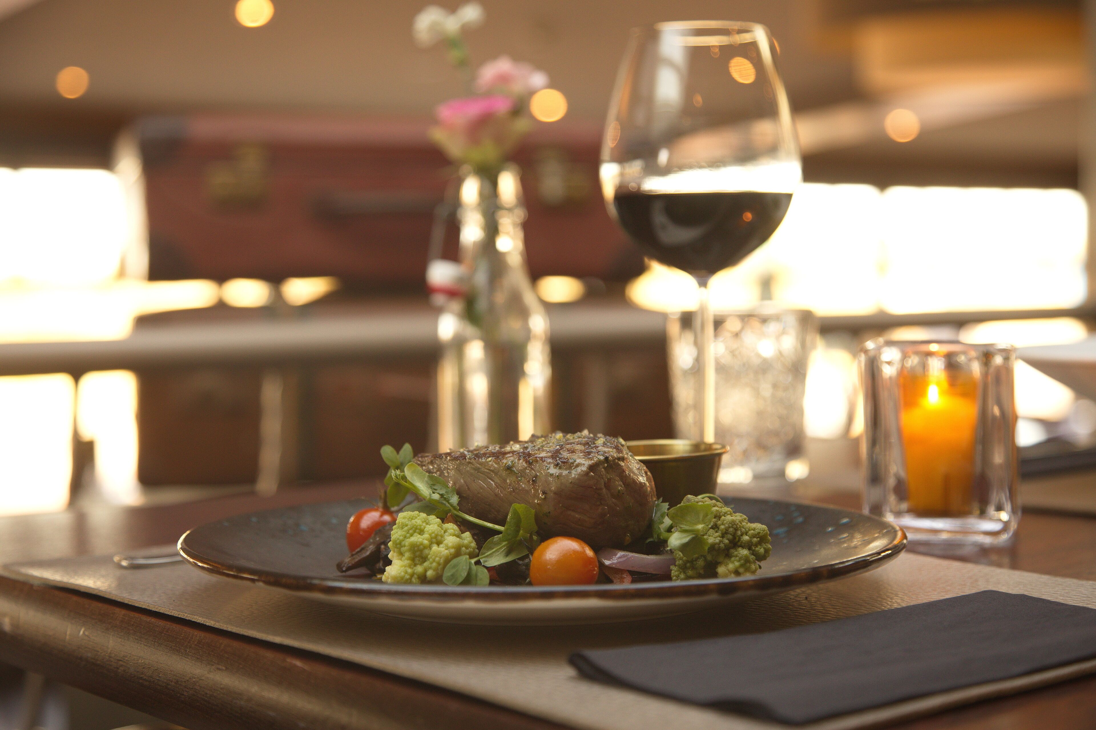 A dining table with a plate of food, a glass of red wine, and a candle.