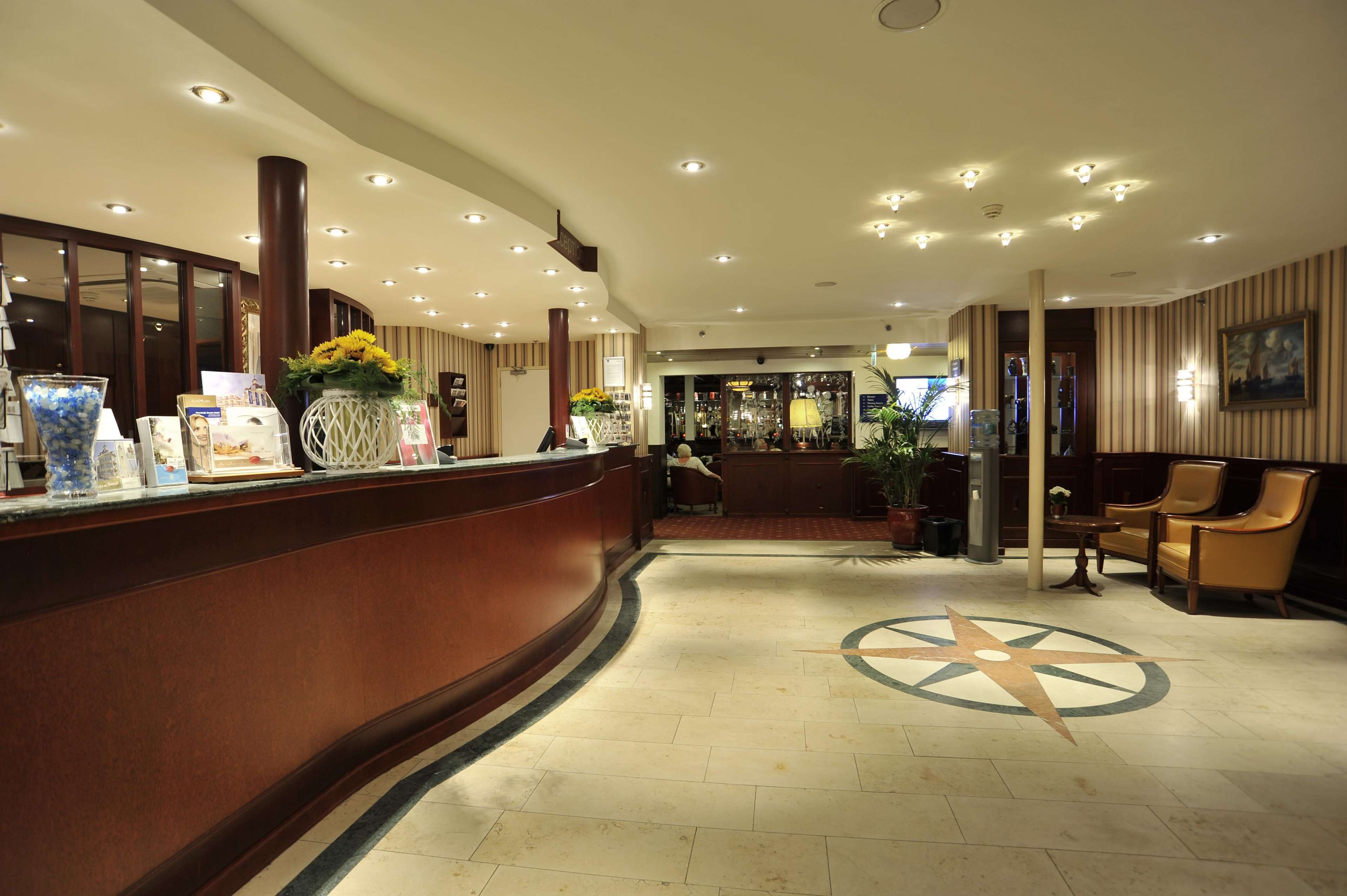 A hotel reception area with a curved reception desk, a large compass floor design, and a seating area with chairs.