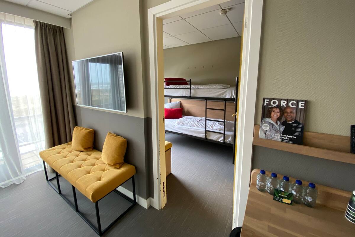A hotel room with a sofa, a TV, bunk beds, a shelf with a magazine, and a water dispenser.