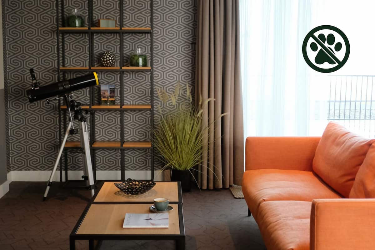 A living room with a telescope on a tripod, a coffee table with a cup and papers, a sofa, and a plant.