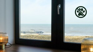 A view from a room with a large window overlooking a beach, a door with a pet prohibition sign, and two lamps on the windowsill. - Two Brothers Noordwijk Beach (Noordwijk)