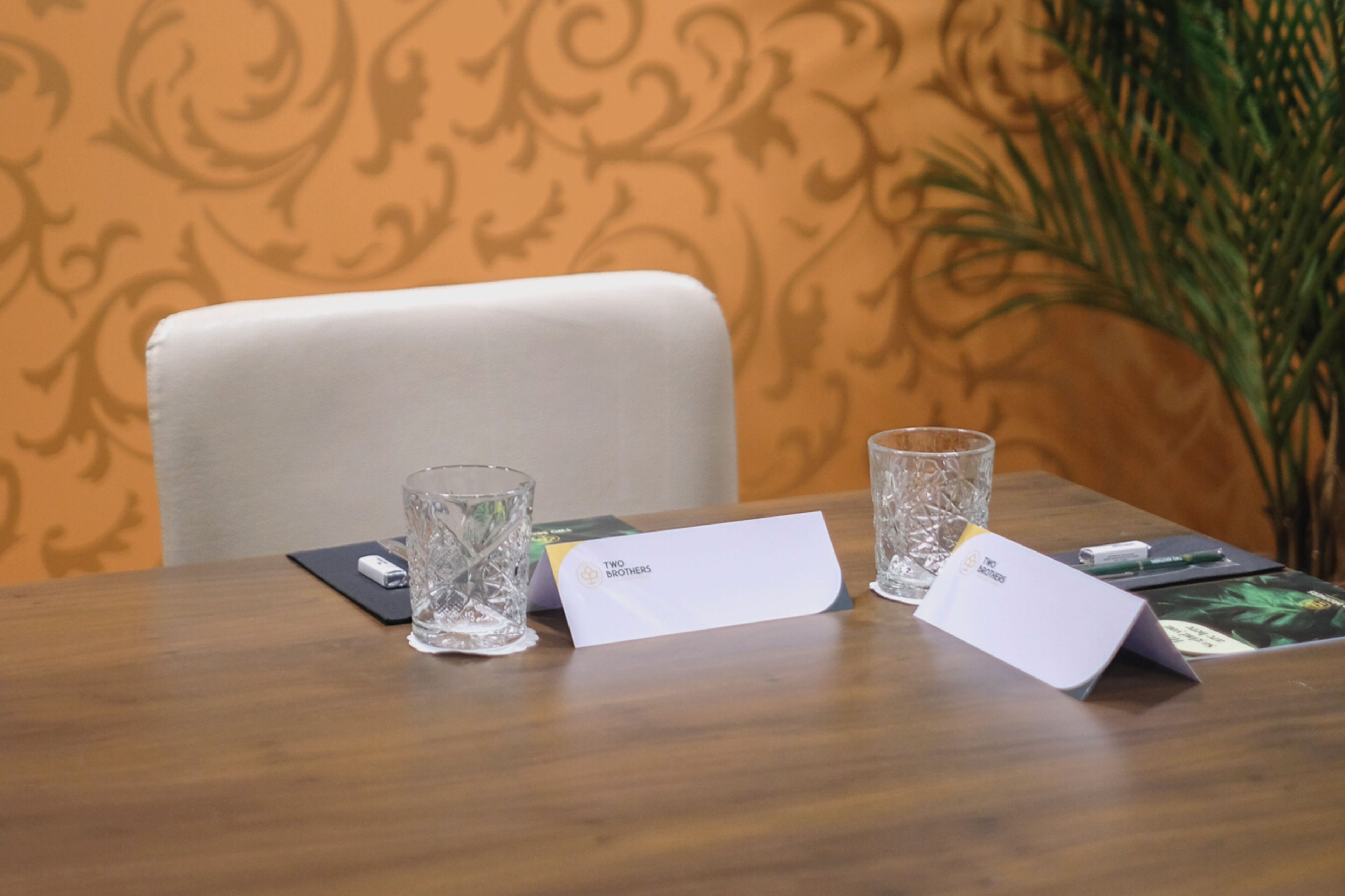 Una mesa de conferencias con tarjetas de nombres, un vaso y una caja etiquetada 'Two Brothers'.