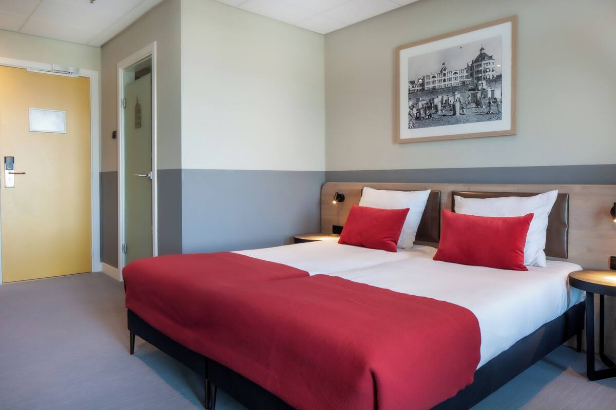 A double bed with red and white bedding, a bedside table, and a framed picture on the wall.