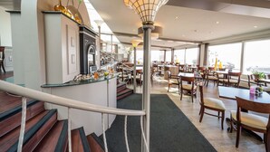 A modern restaurant with a central staircase, dining tables, and chairs. - Two Brothers Noordwijk Beach (Noordwijk)