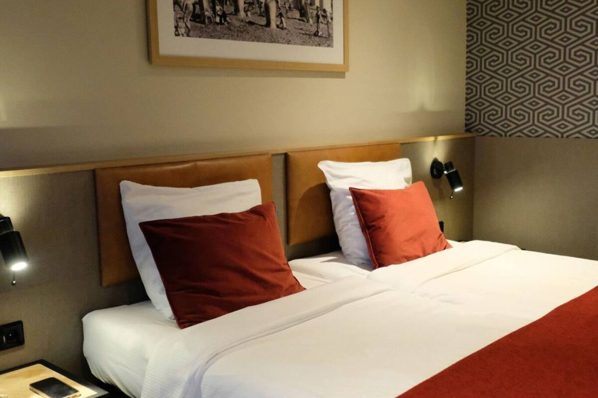 A hotel room with a bed, nightstands, a framed picture on the wall, and patterned wallpaper.
