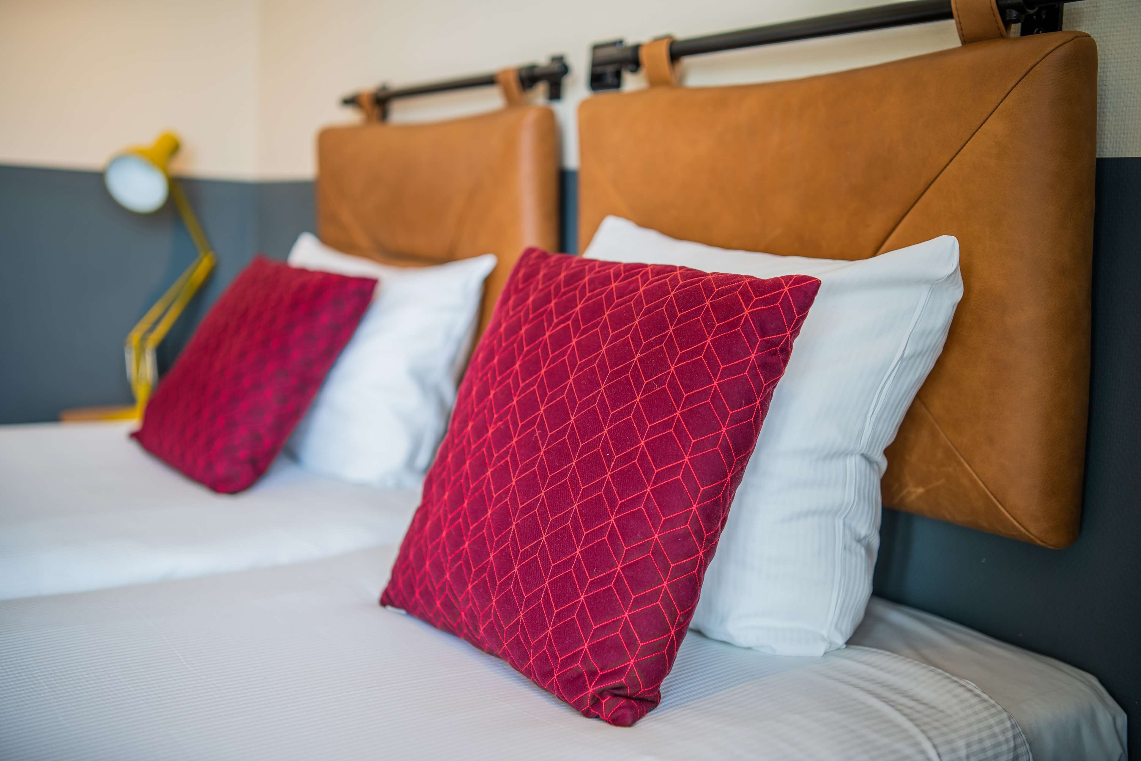 Una cama con cabecera, almohadas y lámpara.