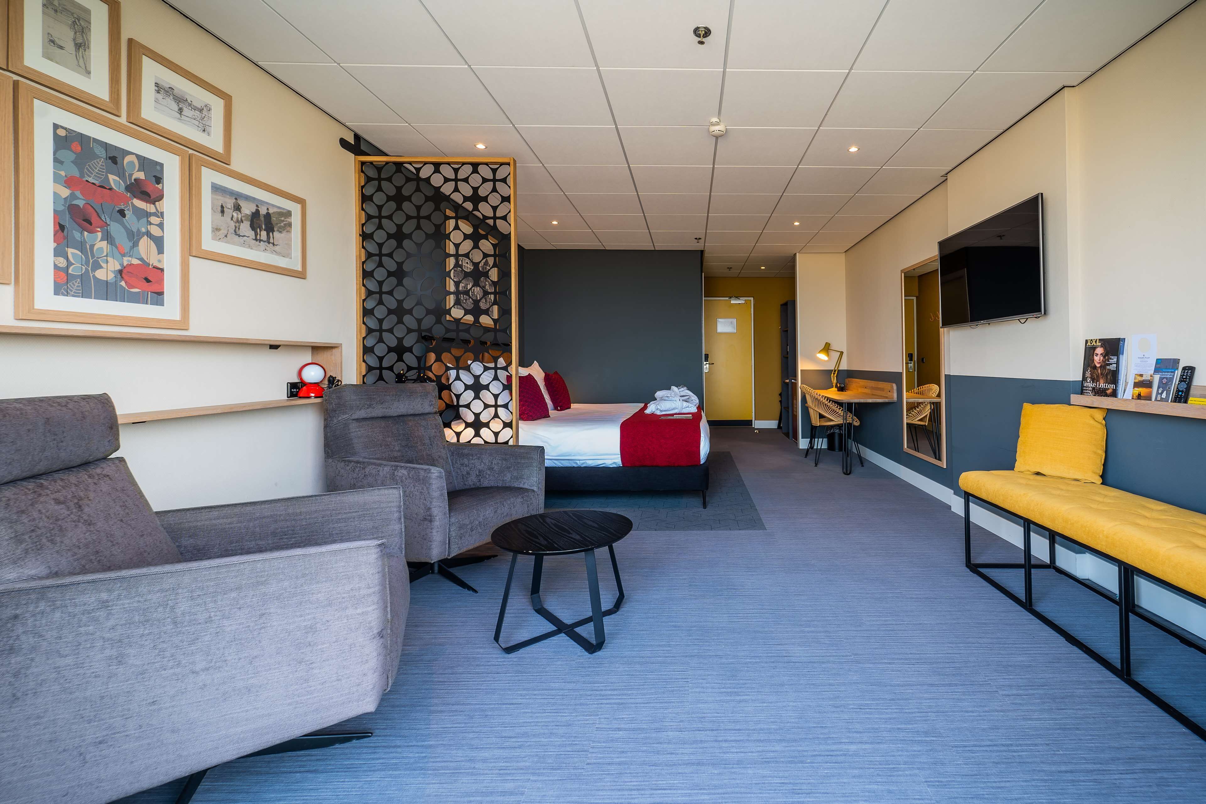 A modern hotel room with a bed, two sofas, a small table, and a TV.