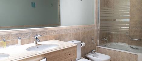 Un baño con dos lavamanos, inodoro y ducha con mampara de vidrio.
