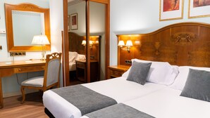 A hotel room with a large bed, a desk, a chair, and a wardrobe.