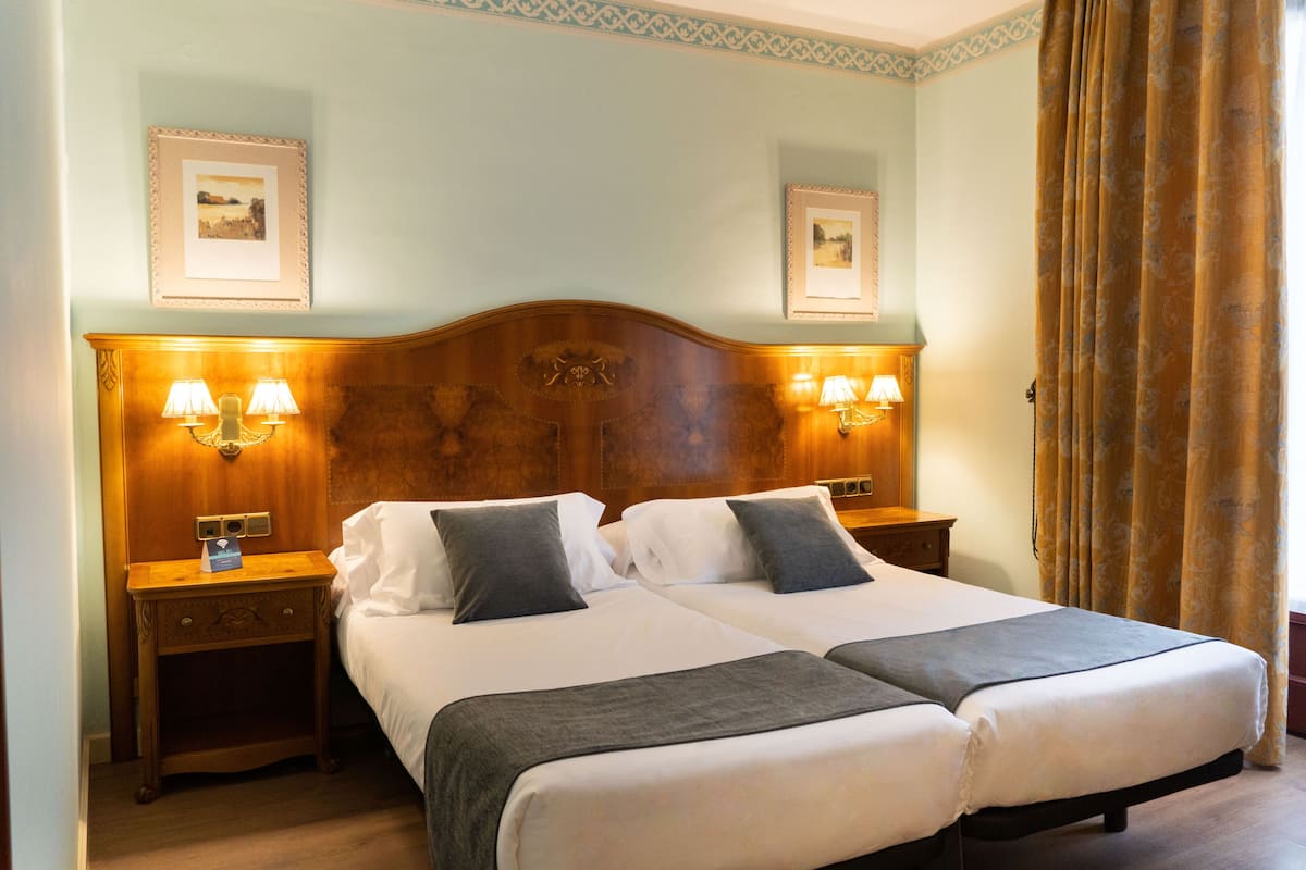 A double bed with two nightstands, each with a lamp, in a room with light blue walls and framed pictures above the bed.