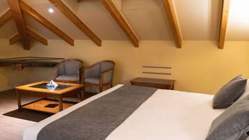 A bedroom with a bed, two chairs, a small table, wooden beams, and a sloped ceiling.