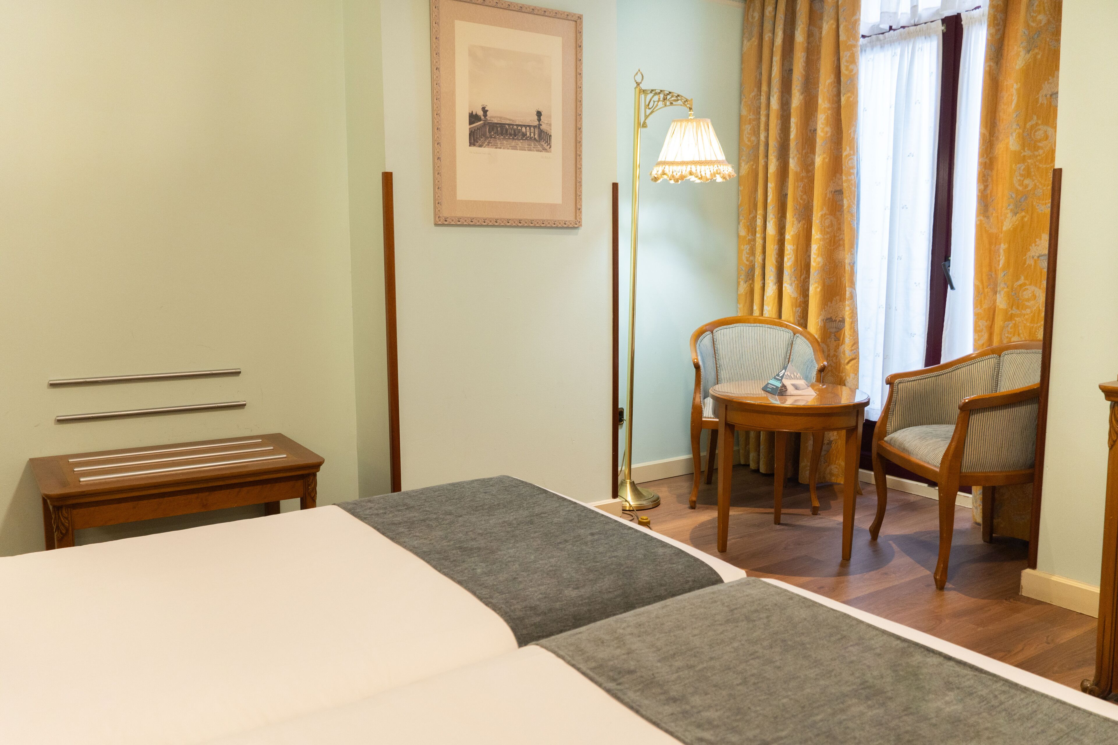 A hotel room with a bed, a desk, a chair, a lamp, and a framed picture on the wall.