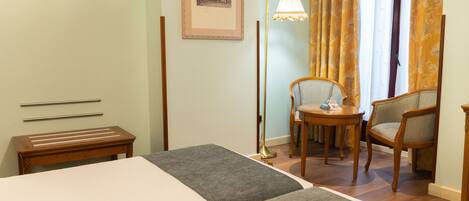 A hotel room with a bed, a desk, a chair, a lamp, and a framed picture on the wall.