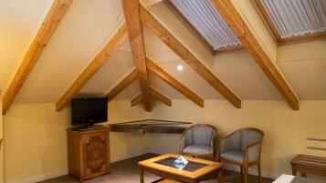 A cozy attic room with wooden beams, a television on a cabinet, two chairs, and a small table.