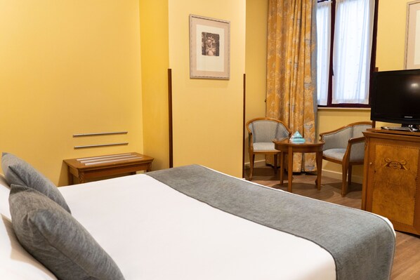Una habitación de hotel con una cama, dos sillas, una mesita, un televisor y una ventana con cortinas.