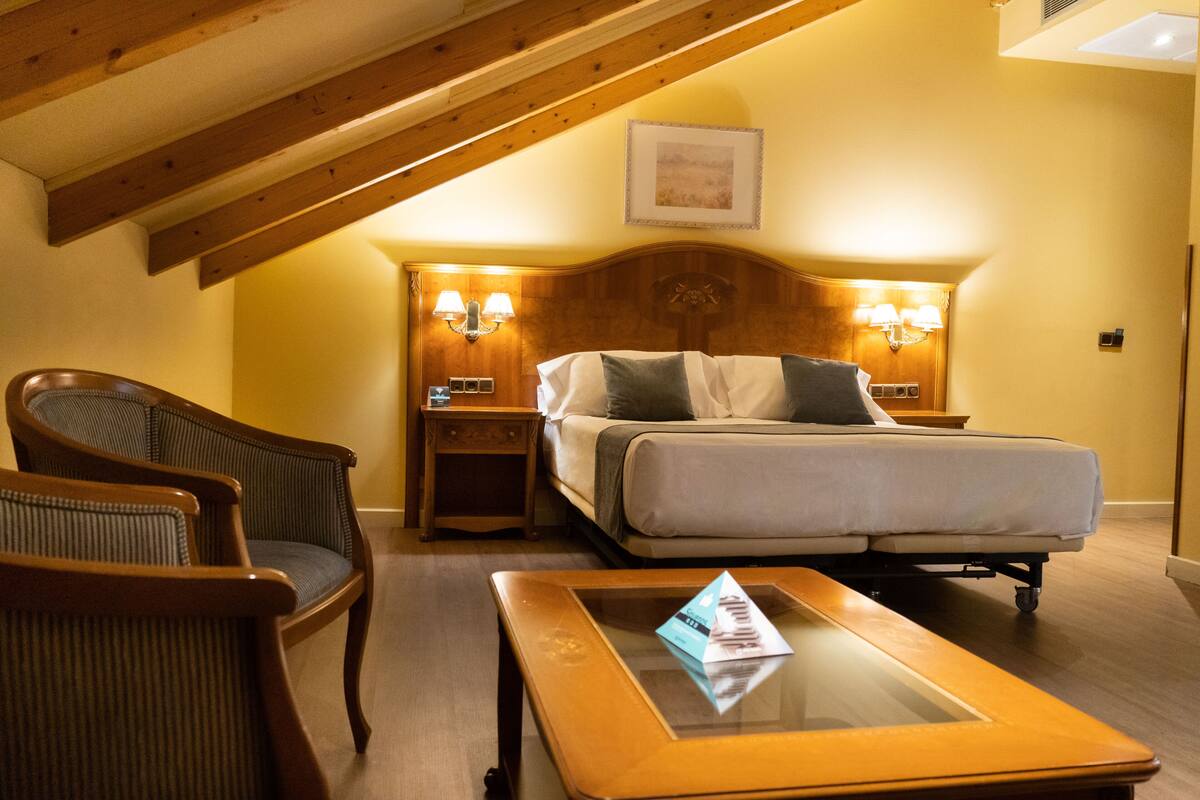 A bedroom with a bed, two nightstands with lamps, a wooden chair, and a glass-top coffee table.