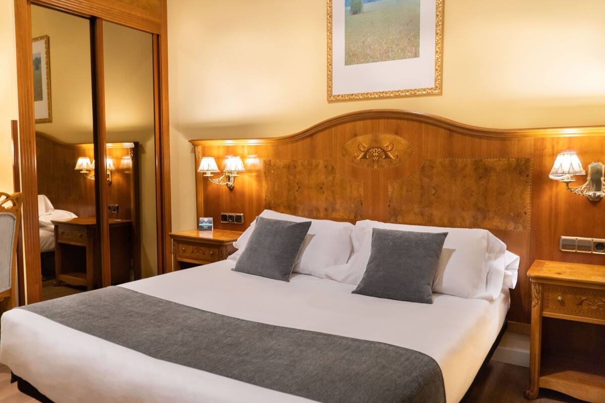 A hotel room with a large bed, wooden headboard, bedside lamps, and a mirror.