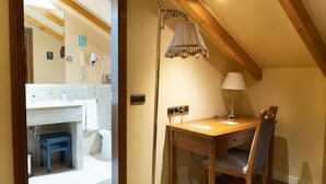 A room with a wooden desk, chair, and a floor lamp. There is a small stool under the desk and a mirror on the wall.