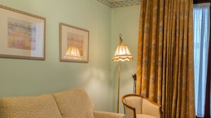 A living room with a sofa, armchair, and coffee table. There is a lamp and a curtain.
