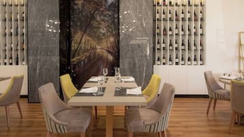 Uma sala de jantar com parede de mármore, adega e mesa posta para quatro pessoas.