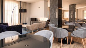 A modern hotel lobby with a round glass table, grey upholstered chairs, a sofa, and a large mirror.
