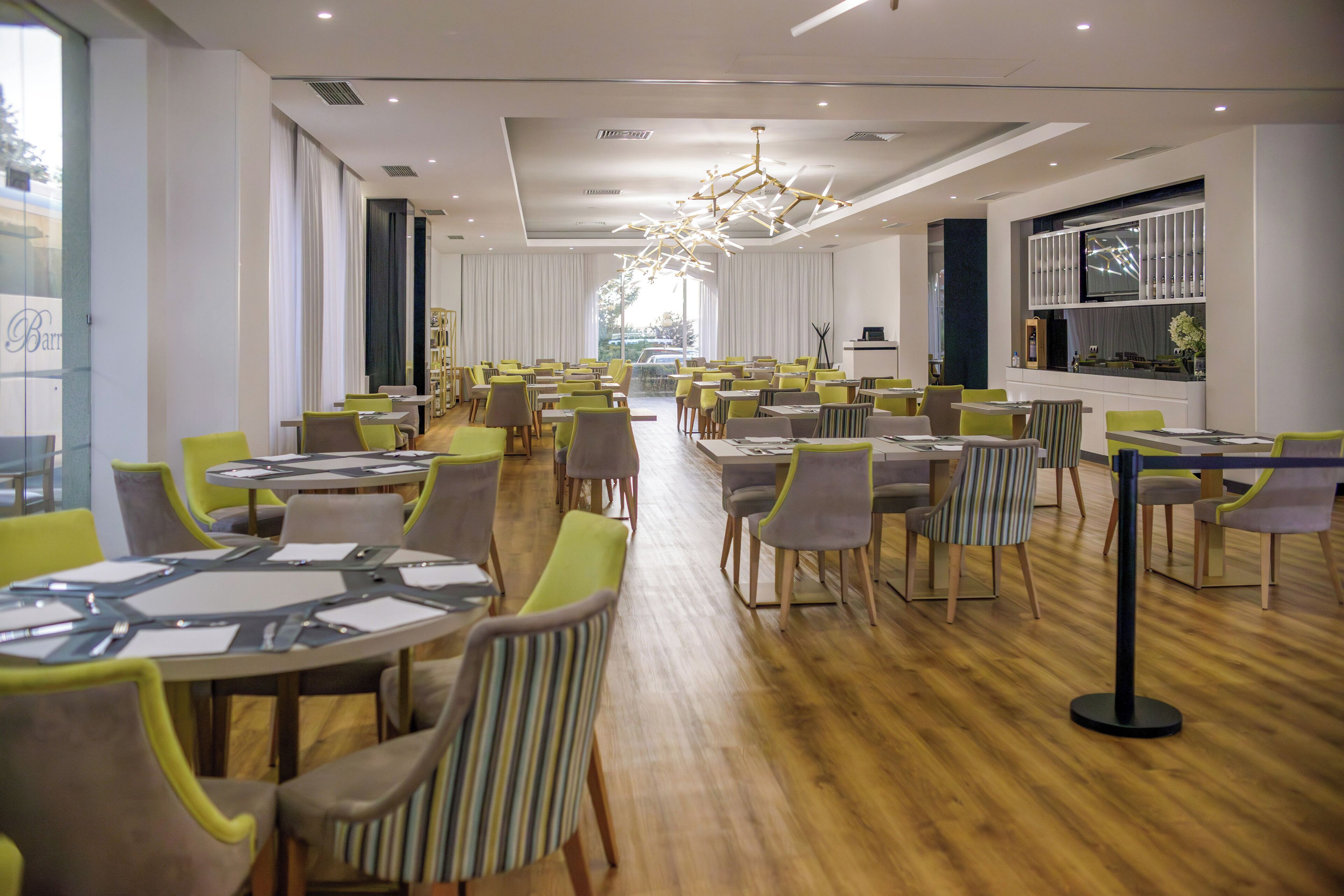 Un comedor espacioso con varias mesas y sillas, una lámpara moderna y grandes ventanales que ofrecen vistas al exterior.