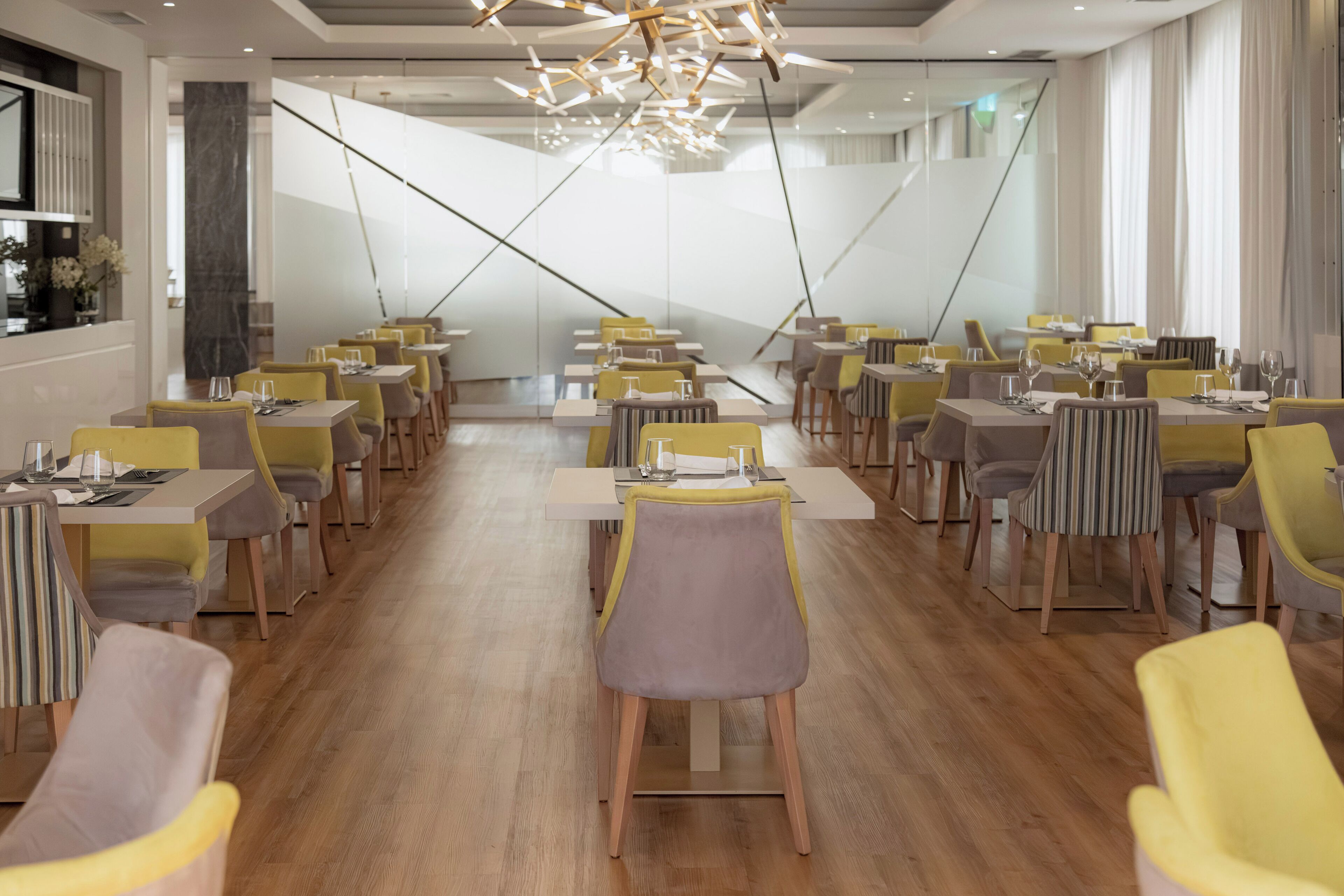 A modern dining area with yellow and grey chairs, wooden tables, and a contemporary chandelier.