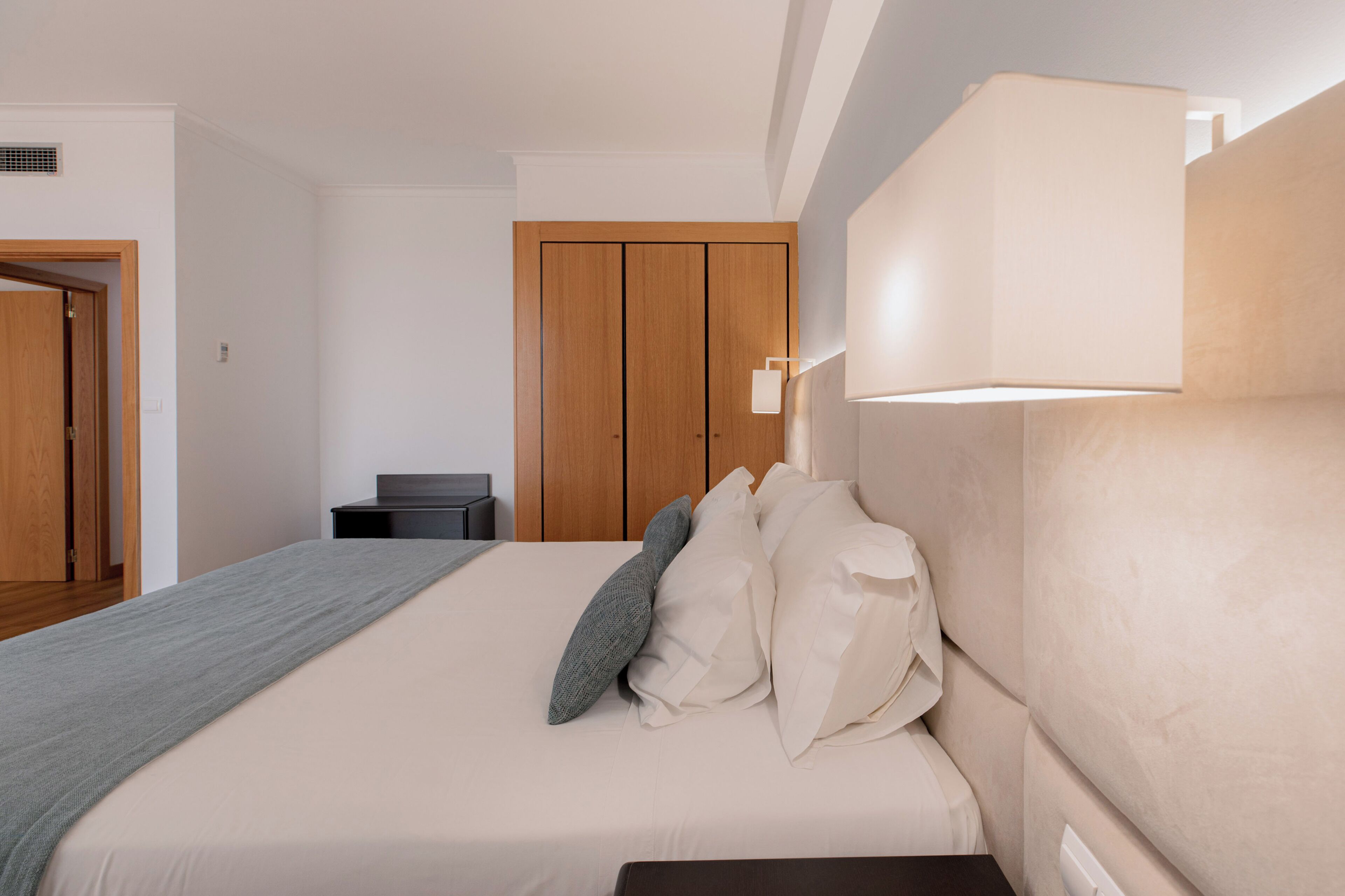 A bedroom with a bed, bedside table, lamp, wardrobe, and a door.