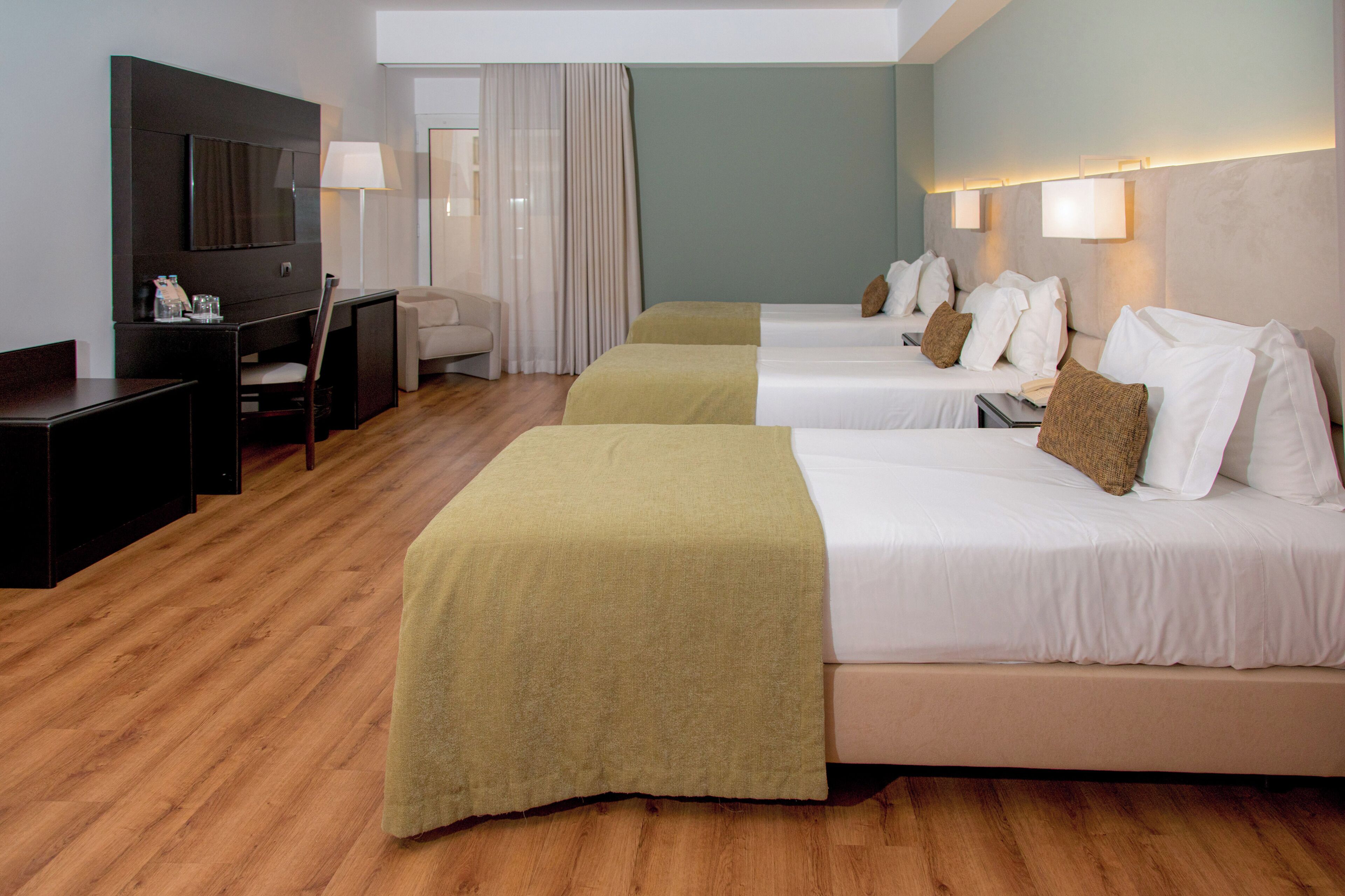 Habitación de hotel con dos camas, un escritorio, una silla, un televisor y una ventana con cortinas.