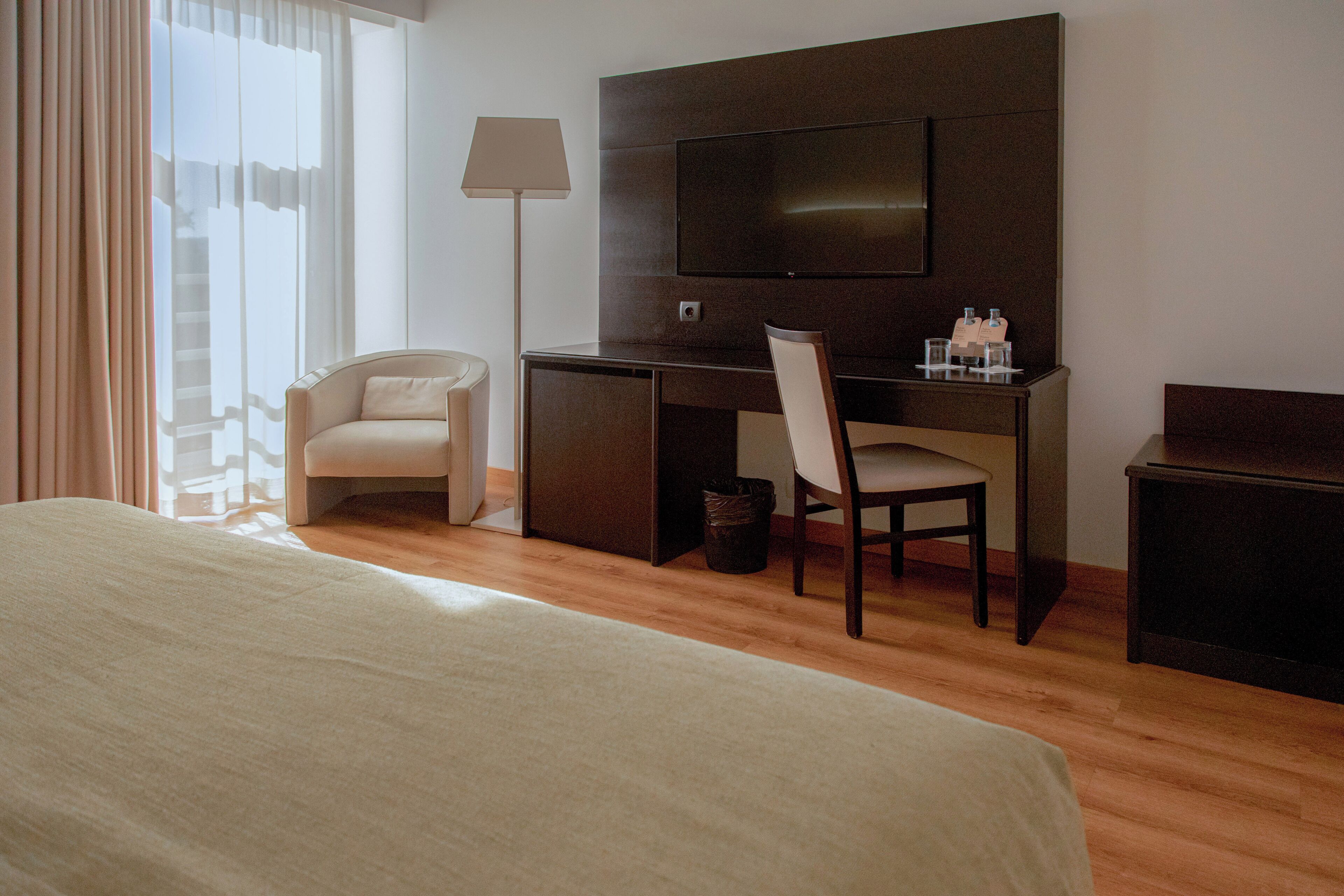 Una habitación de hotel con una cama, un escritorio con una silla, un televisor y una lámpara.