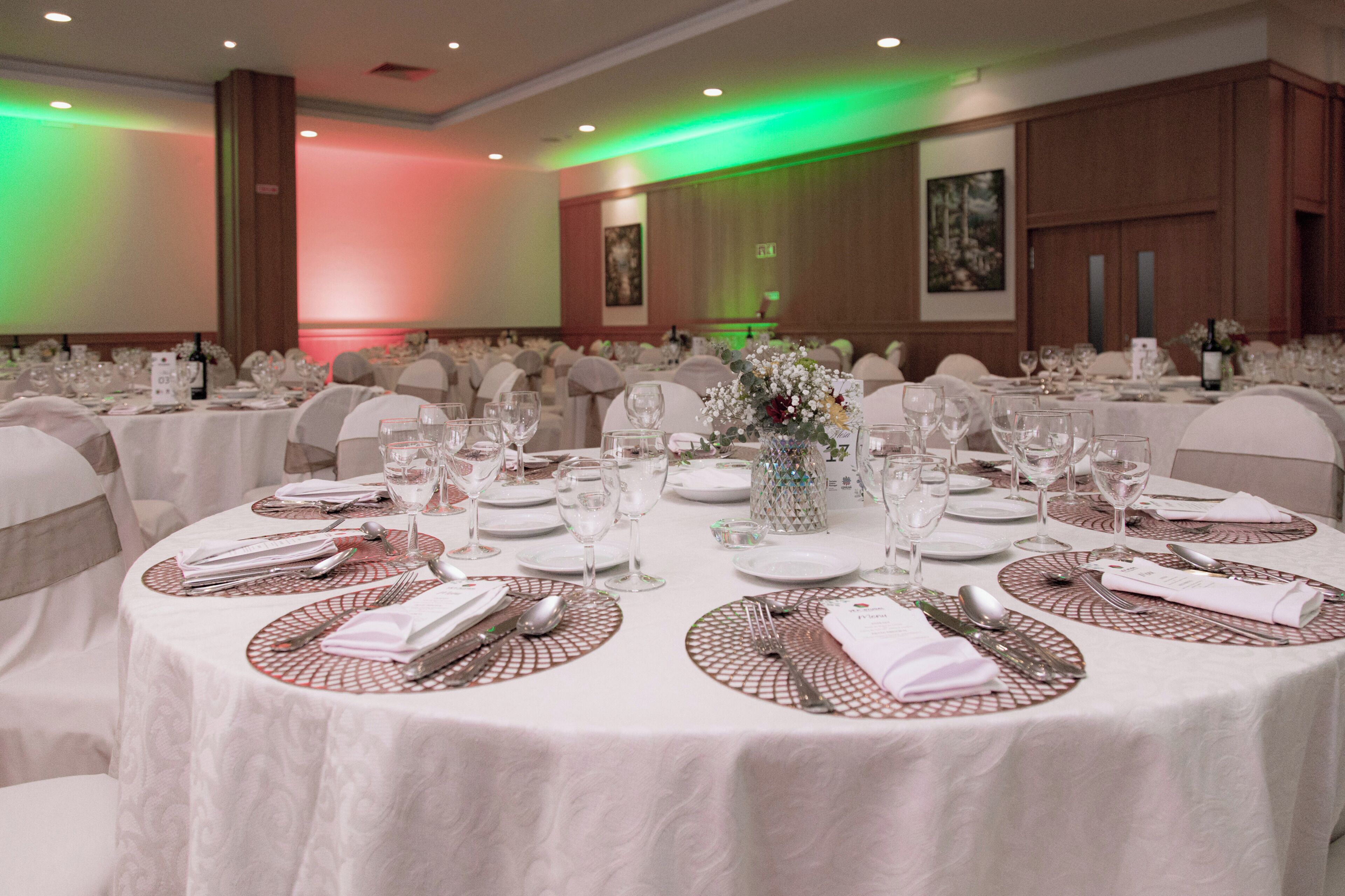 A banquet hall with round tables set for a formal event, featuring white tablecloths, placemats, and glassware.