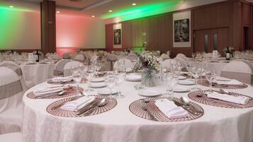 A banquet hall with round tables set for a formal event, featuring white tablecloths, placemats, and glassware.