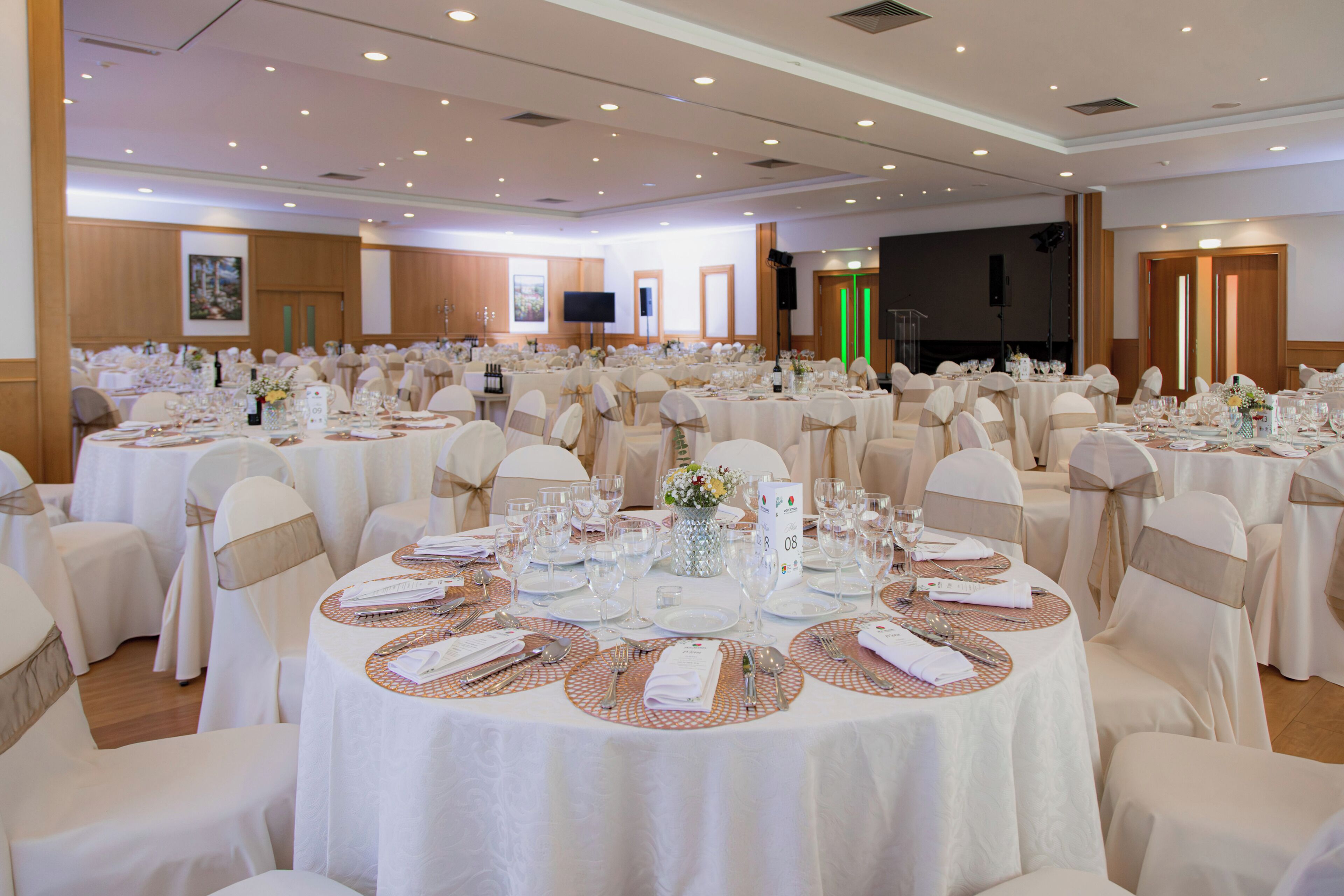 A banquet hall with round tables, chairs, and a stage.