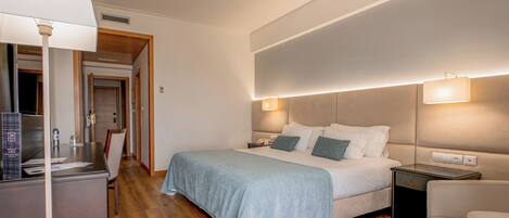 A hotel room with a bed, bedside tables, a desk, and a chair.
