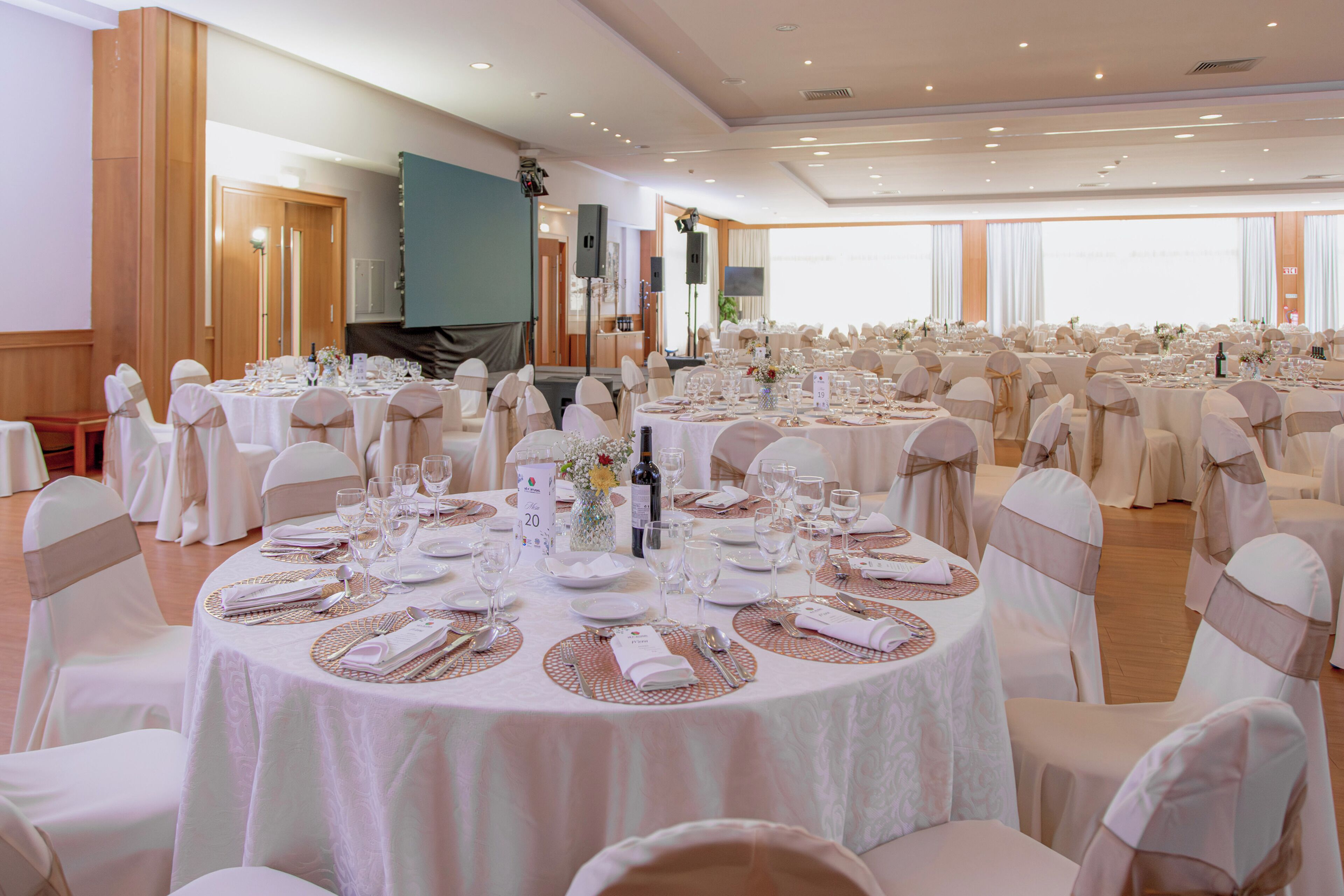 Un salón de banquetes con mesas redondas, manteles blancos y sillas con cintas.