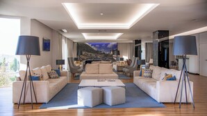 A spacious living room with a large sofa set, a coffee table, and a view of a mountainous landscape through a large window.