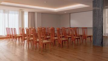 A conference room with wooden chairs arranged in rows, a large screen, and a marble pillar.