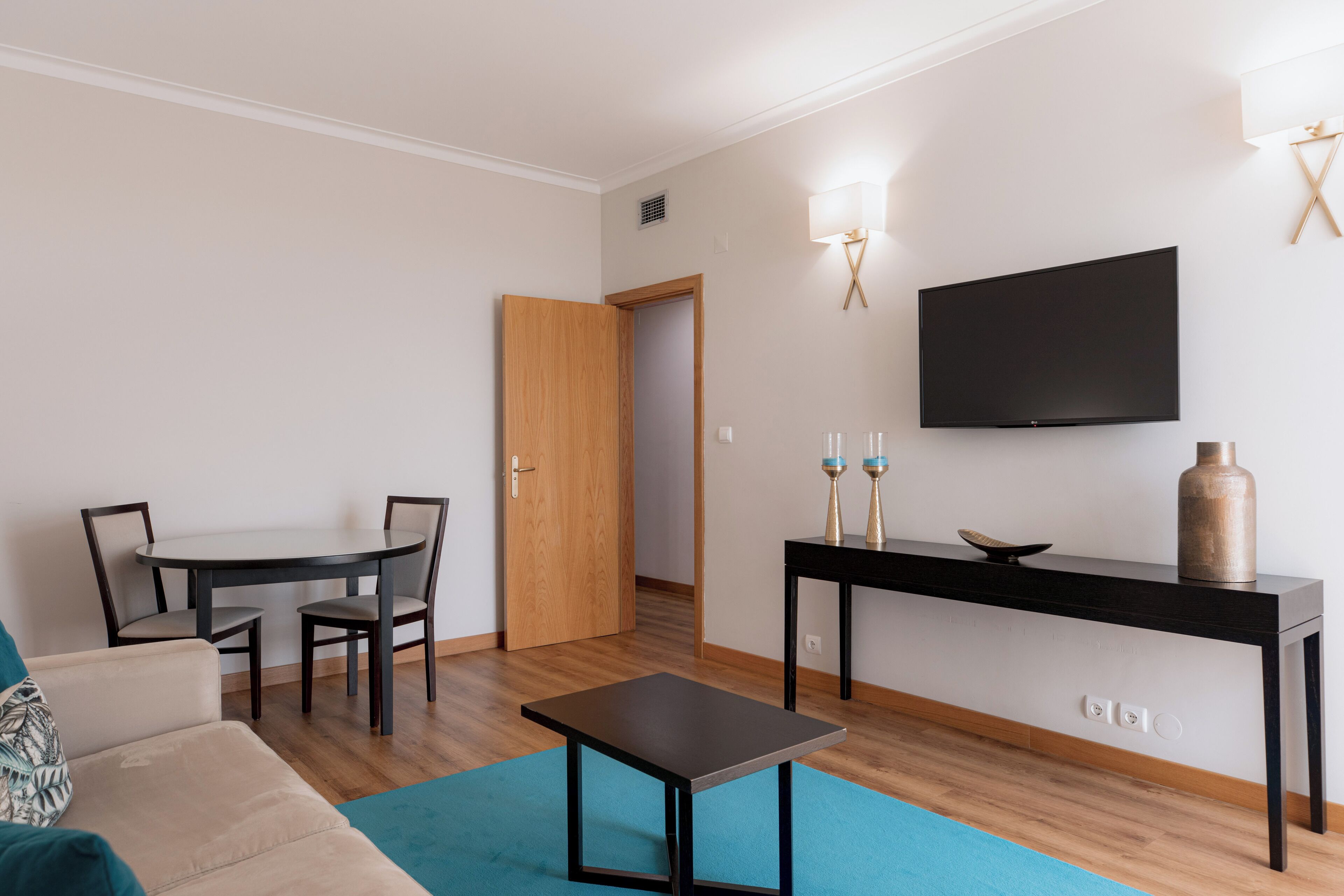Una sala de estar moderna con un sofá, una mesa de centro, una mesa de comedor con sillas, un televisor montado en la pared y un aparador con adornos.