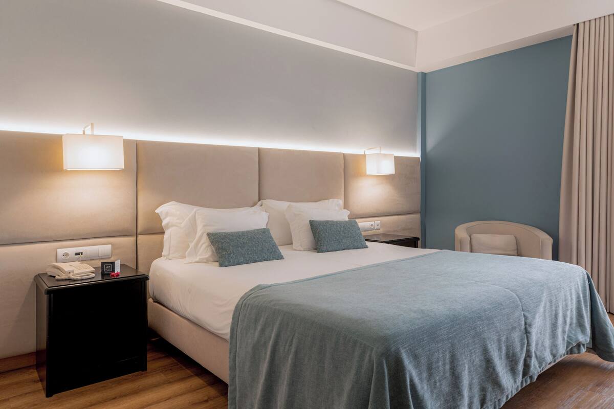 Habitación de hotel con cama, lámparas de noche, mesita de noche y un sillón.